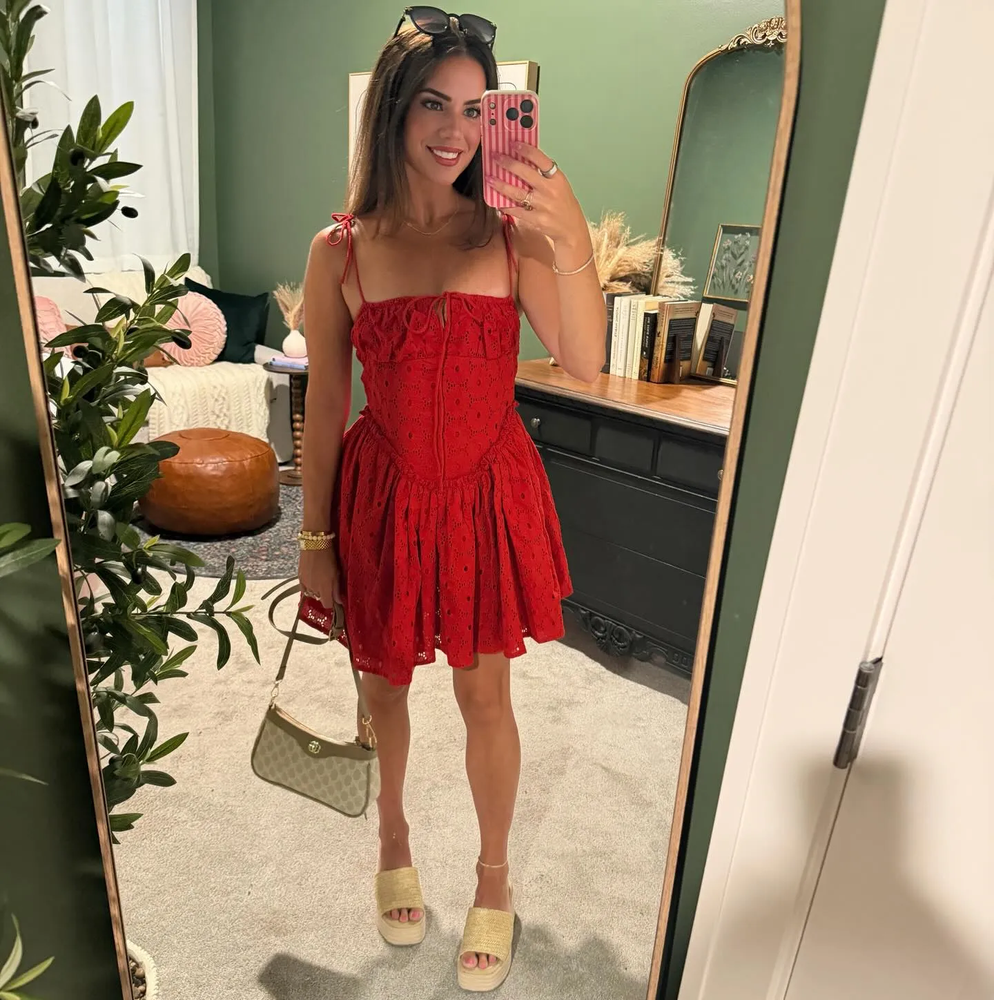 Susanne in a bright red eyelet mini dress with tie straps, tan raffia platform sandals and a neutral shoulder bag, mirror selfie in her green dressing room