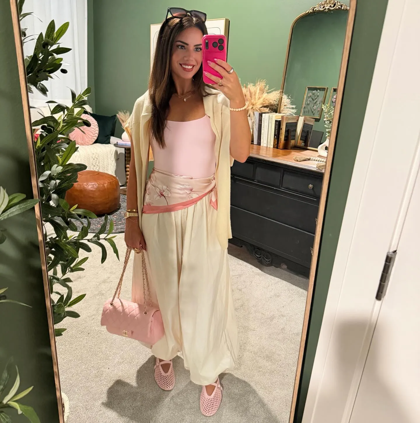 Susanne in a light pink bodysuit and cream balloon-hem pants with a pink floral scarf tied at the waist, cream sweater on her shoulders, pink bag and mesh flats