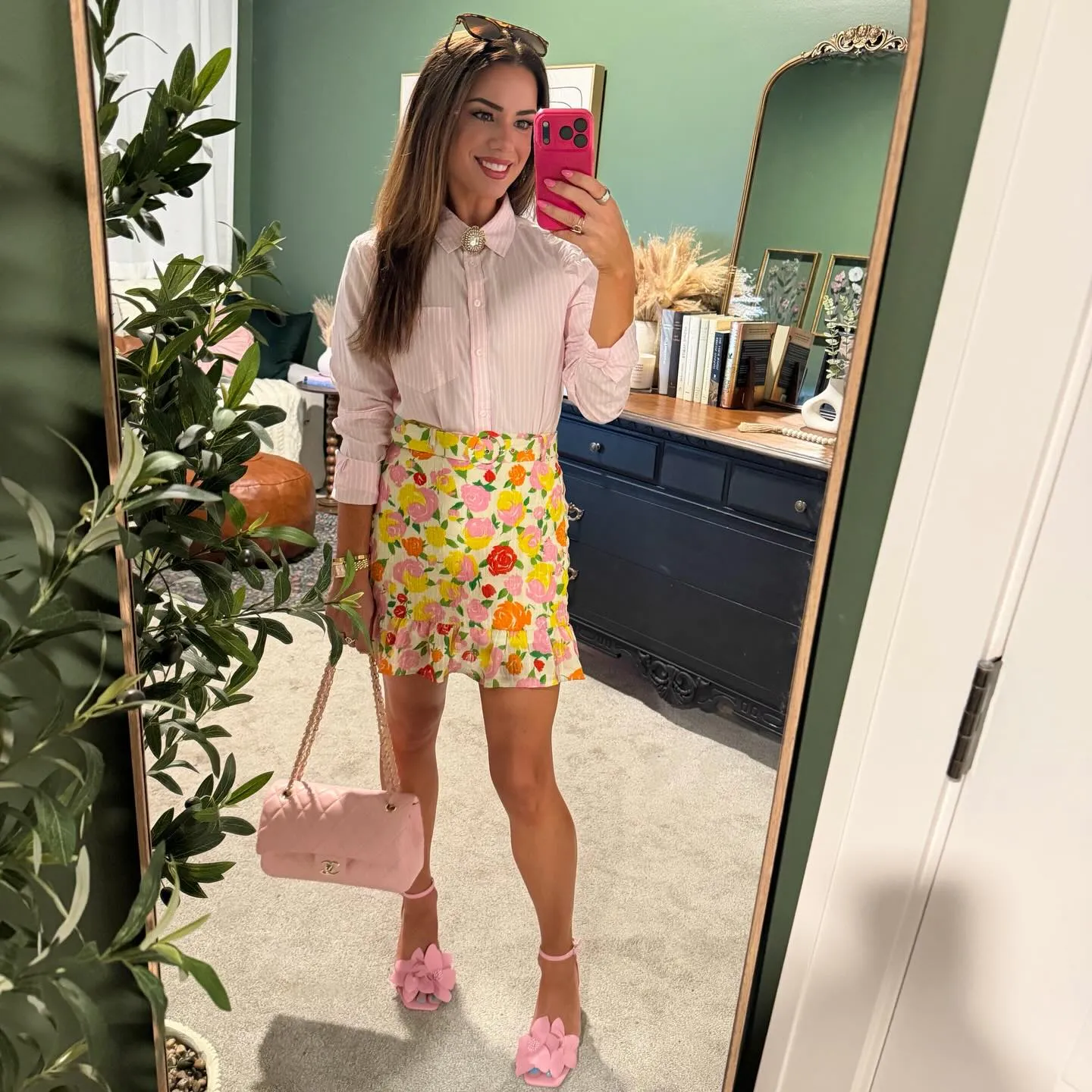 Pink and white striped button-down with a gold brooch, a floral mini skirt in pink, yellow and orange, pink flower heels and a pink quilted chain bag.