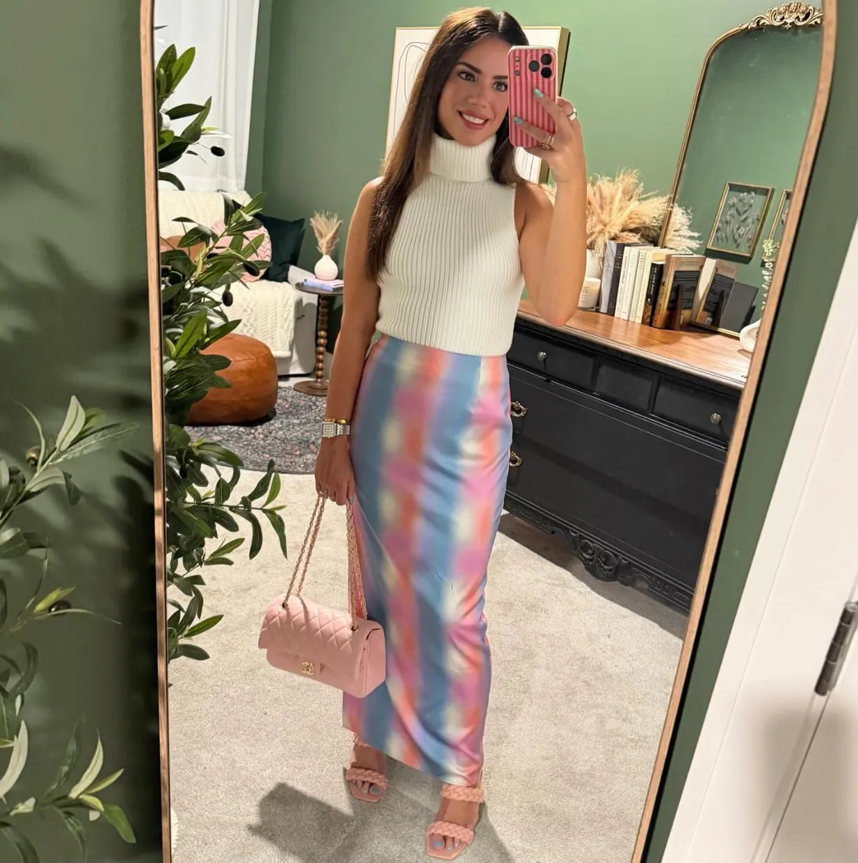 Susanne smiling in her mirror, wearing a white knit and a pastel watercolor skirt.