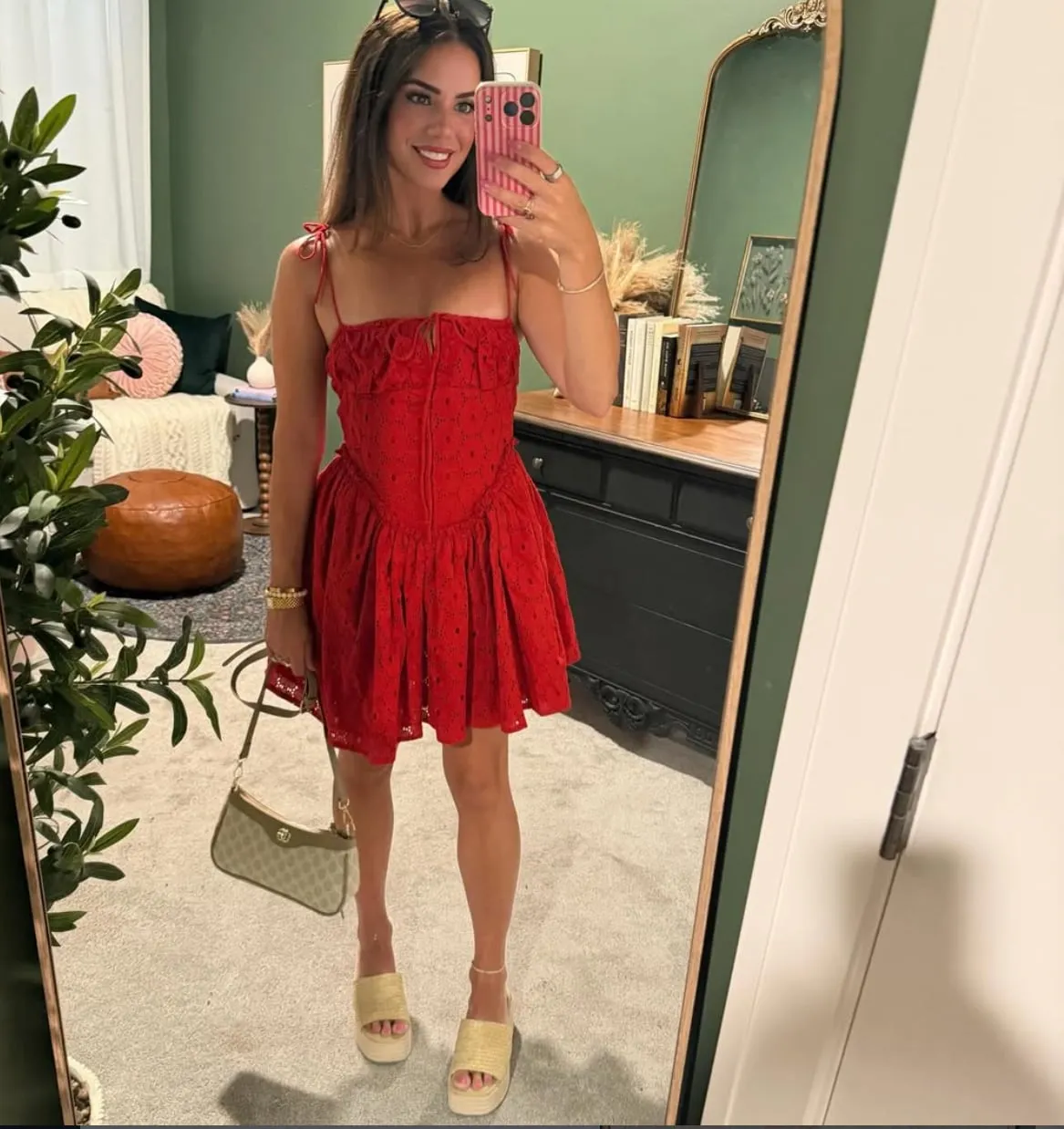 Susanne in a mirror wearing a red eyelet mini dress with tie straps, holding a neutral shoulder bag, with woven platform sandals.